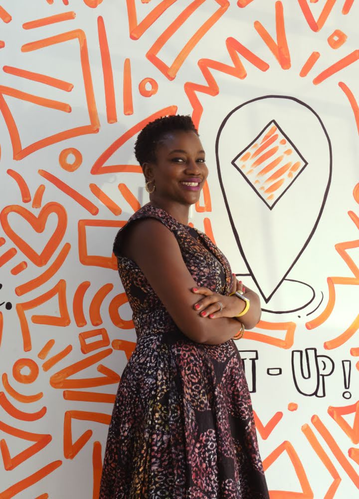 Portrait d'Adenike Adeyemi debout devant un mur aux motifs orange et aux dessins en forme de cœur