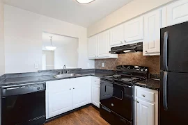 Modern kitchen in an apartment with white cabinets, black appliances, and dark countertops.