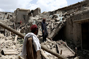 Afghan men stand on the debris of a house that was destroyed by an earthquake in Gayan, Afghanistan, June 23, 2022.  