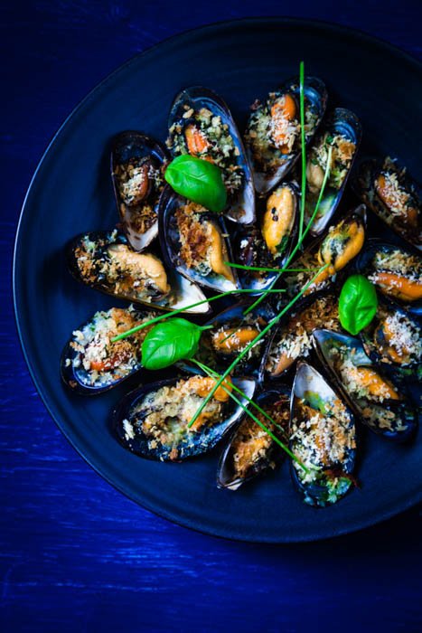 Ovrhead food composition of mussels graitnee on blue plate on an indigo background