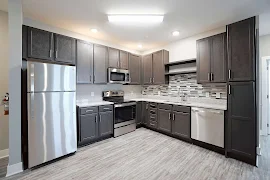 Kitchen with dark brown cabinets, stainless steel appliances, granite countertops, grey tone backsplash, light wood floors