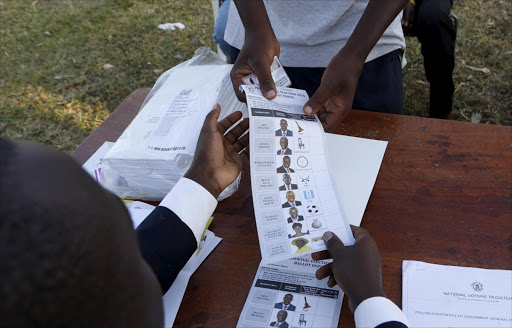 A polling assistant issues a ballot paper to a voter at a polling station during elections in Kirihura in western Uganda February 18, 2016. Ugandans start casting votes on Thursday to decide whether to give Yoweri Museveni, in power for three decades, another term in office. REUTERS/James Akena