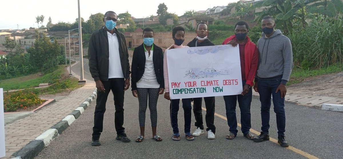 6 rebels stand in a street with a banner: Pay your climate debts, compensation now.