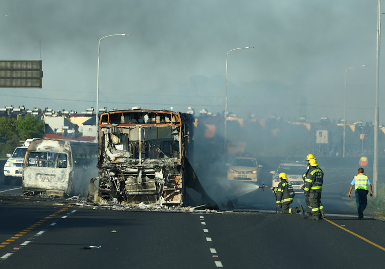 Firefighters hose down a bus set alight during a protest by taxi operators in Cape Town on Thursday.