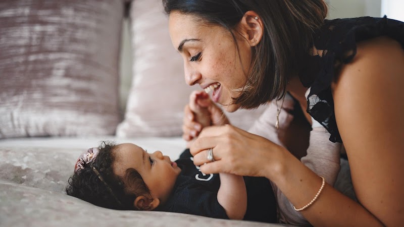 Woman smiling down at newborn in black onesie and holding baby's hands.