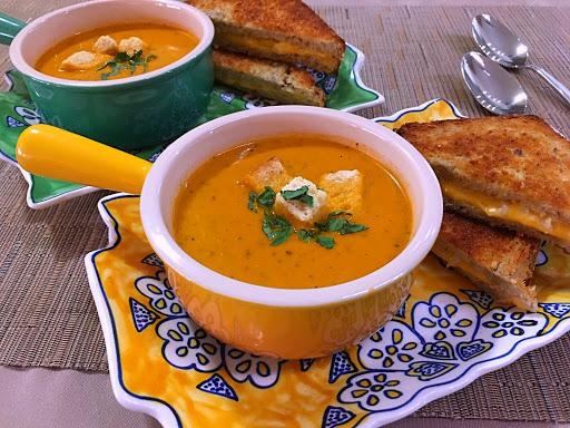 Two bowls of tomato soup along with grilled cheese sandwiches.