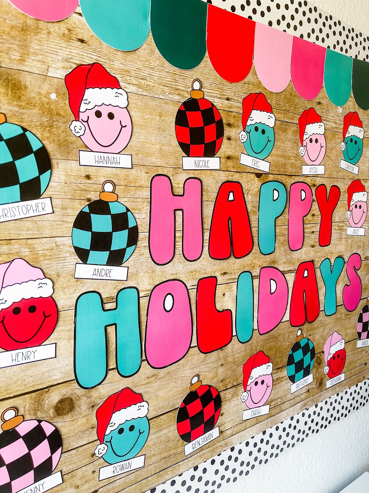 This image shows a christmas bulletin board with the letters to spell happy holidays and smiley faces and ornaments with students names on them.