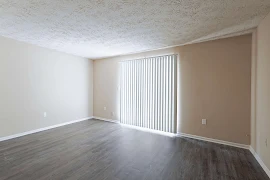 Living room with dark wood-inspired floors, neutral walls, light trim, and a sliding glass door with light vertical blinds.