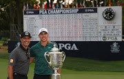 Brooks Koepka of the United States poses with Claude Harmon and the Wanamaker Trophy on the 18th green after winning the 2018 PGA Championship with a score of -16 at Bellerive Country Club on August 12, 2018 in St Louis, Missouri. 