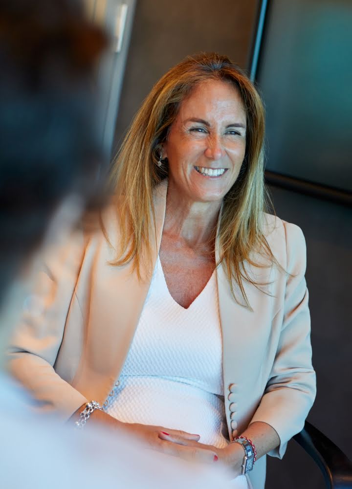 Portrait de Carmen Correa assise dans son bureau, souriant à son équipe