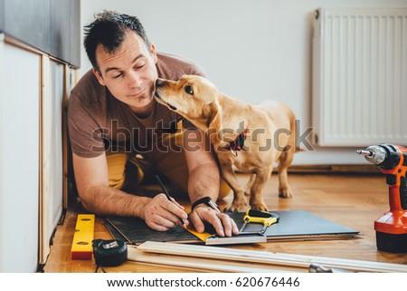 A builder working on a home renovation while a cute dog distracts him by licking his face