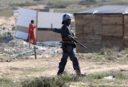 A public order policeman armed with a shotgun stands guard as shacks are demolished in Dunoon, Cape Town, on April 25 2019.