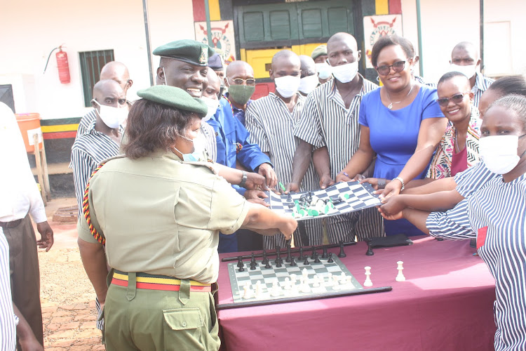 Prison officers and prisoners receive a chess board from Chess Kenya's Saphinah Kenyando (in blue)