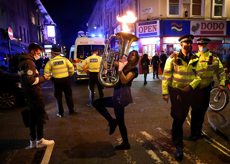 A street performer plays a musical instrument in protest against lockdown measures near police officers wearing protective face masks as pubs close ahead of the lockdown in Soho, London, Britain, November 4, 2020.