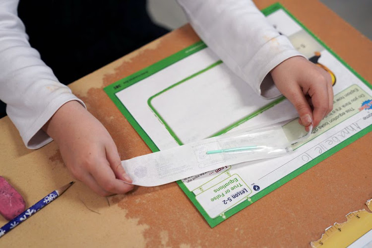 A child opens a testing swab at her desk so she can swab and test herself for COVID-19 to prevent the spread of coronavirus disease (COVID-19) in the classroom at South Boston Catholic Academy in Boston, Massachusetts, U.S., January 28, 2021.