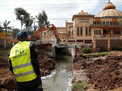 A private security officer stands guard as heavy machinery demolishes a bridge near the Oshwal Centre in Westlands, Nairobi, Kenya, August 14, 2018. /REUTERS