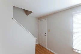 Entry area with light paneled door at the base of a staircase with neutral walls and wood-inspired floors and light trim.