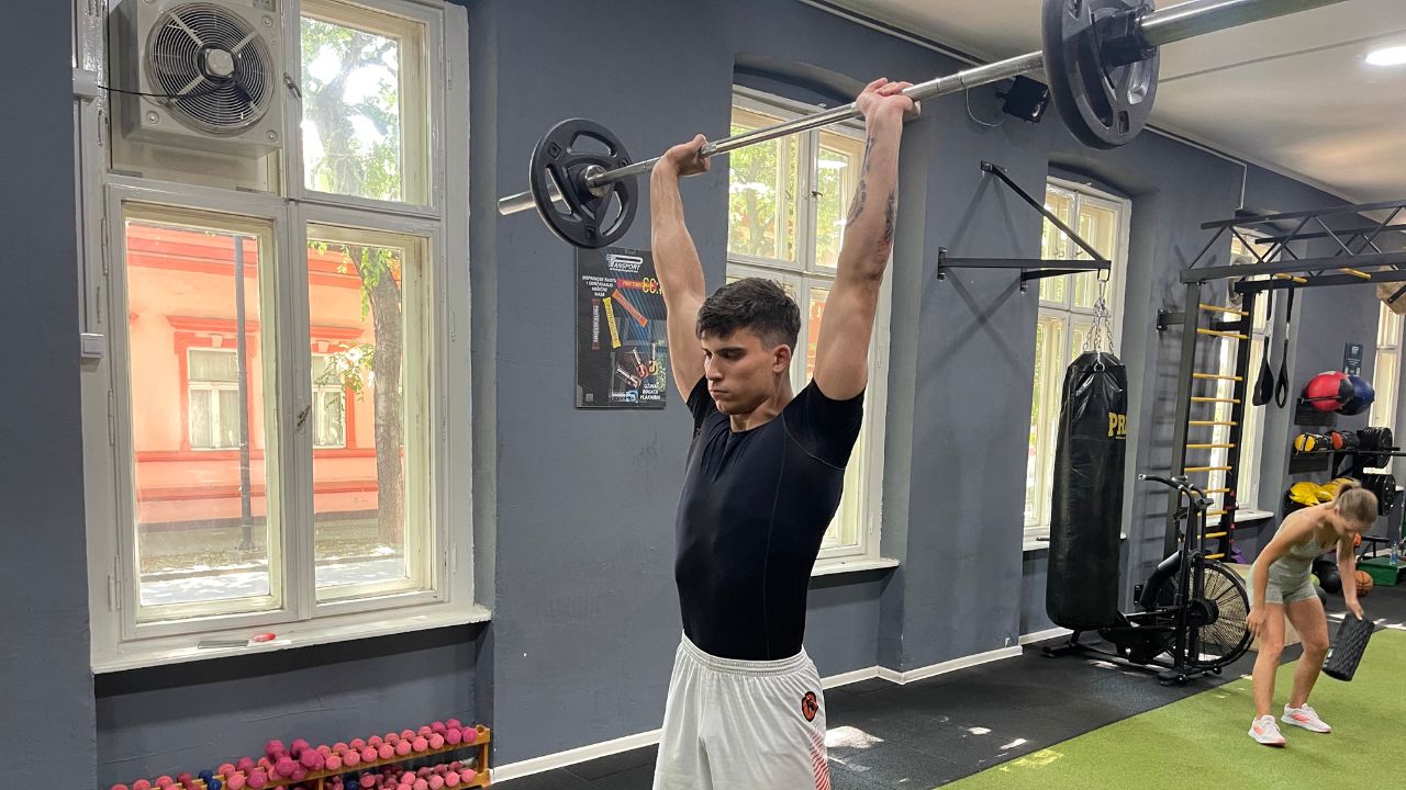 Vanja performs a barbell overhead press.