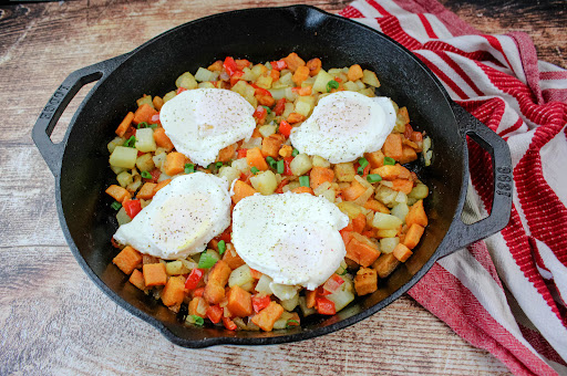 A cast iron skillet with Sweet Potato Hash and over-easy eggs.