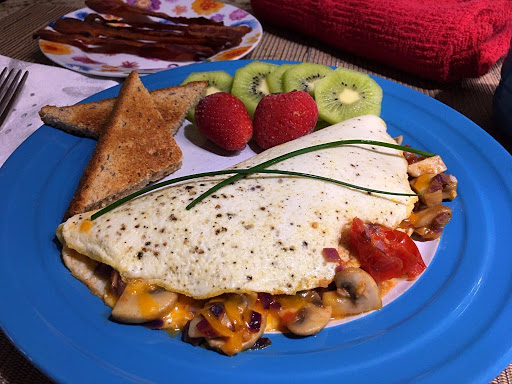 An omelet sitting on a plate with strawberries, kiwifruit slices and toasts.