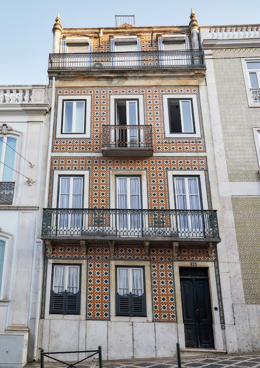 Typical of the buildings of central Lisbon, the narrow façade is clad in exuberantly patterned tiles and features cast-iron balconies on the upper floors.