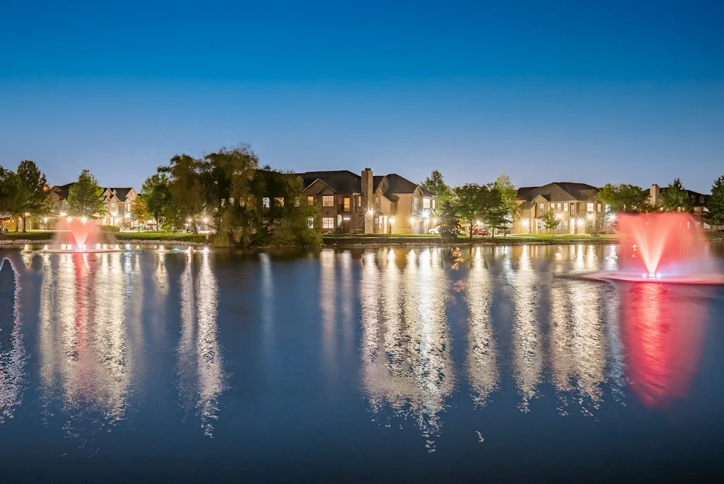 Village at Lionsgate's on-site lake with red fountains surrounded by lit up apartment buildings at night