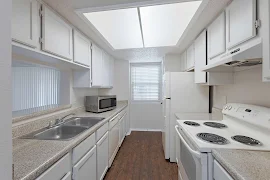 Kitchen with white appliances including a dishwasher, fridge, & coil eye range. Plus white cabinets & a large overhead light