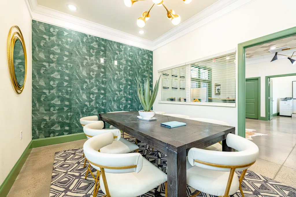 Modern apartment complex lobby with stylish chairs, a wooden table, patterned floor, and green accent wall.