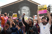 People hold Black Lives Matter posters gathering at a repaired mural of England footballer Marcus Rashford by the artist known as AKSE_P19, which is displayed on the wall of a cafe on Copson Street, Withington, Manchester, on July 13, 2021. AKSE_P19 repaired the image after it was defaced by vandals in the aftermath of England's Euro 2020 final defeat to Italy two days before. Rashford and other Black players in England's national football team were the target of racist abuse, largely on social media, after the team's Euro final defeat.