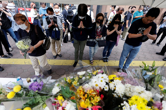 People pray next to flowers laid at the site where late former Japanese Prime Minister Shinzo Abe was shot while campaigning for a parliamentary election, near Yamato-Saidaiji station in Nara, Japan, on July 9, 2022.