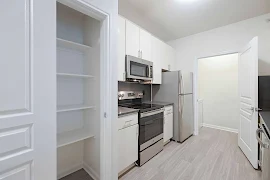 Modern apartment kitchen with white cabinetry, stainless steel appliances, and built-in shelving.