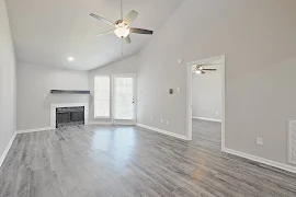 Spacious, well-lit apartment interior with hardwood floors, ceiling fan, fireplace, and glass door leading to another room.