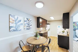 Furnished dining room and kitchen with light gray walls, white trim, light wood plank flooring, and mounted lights