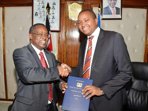 Planning PS Julius Muia shakes hands with Devolution PS Irungu Nyakeru