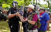 An armed far-right militia member fist-bumps a police officer in riot gear as various militia groups stage rallies at the Confederate memorial at Stone Mountain, Georgia, US, on August 15 2020. 