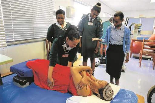 NEW SKILLS: John Bisseker Grade 11 pupils Khanya Nqwensio and Zizipho Dweba look on while their peer Roseline Adams helps patient Ntombencini Gqadushe, guided by physiotherapist Pakama Ramontseng. About 40 girls were shown how various departments in the hospital function and allowed to interact with patients Picture: ALAN EASON