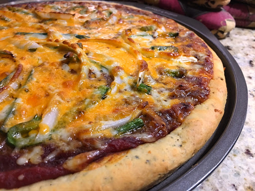 Homemade pizza with toppings sitting on a pizza pan on the kitchen counter.