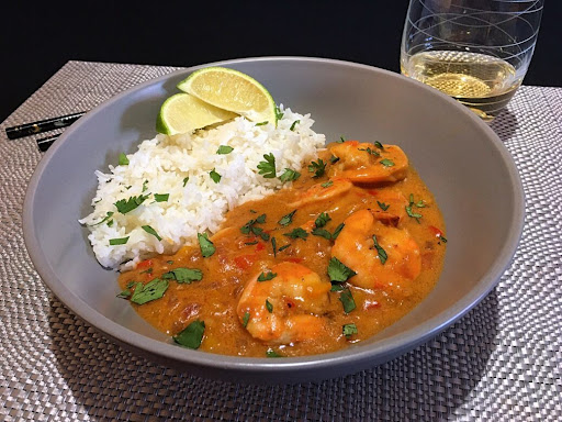 A bowl of delicious Thai Curry Shrimp along with white rice and a couple lime wedges.