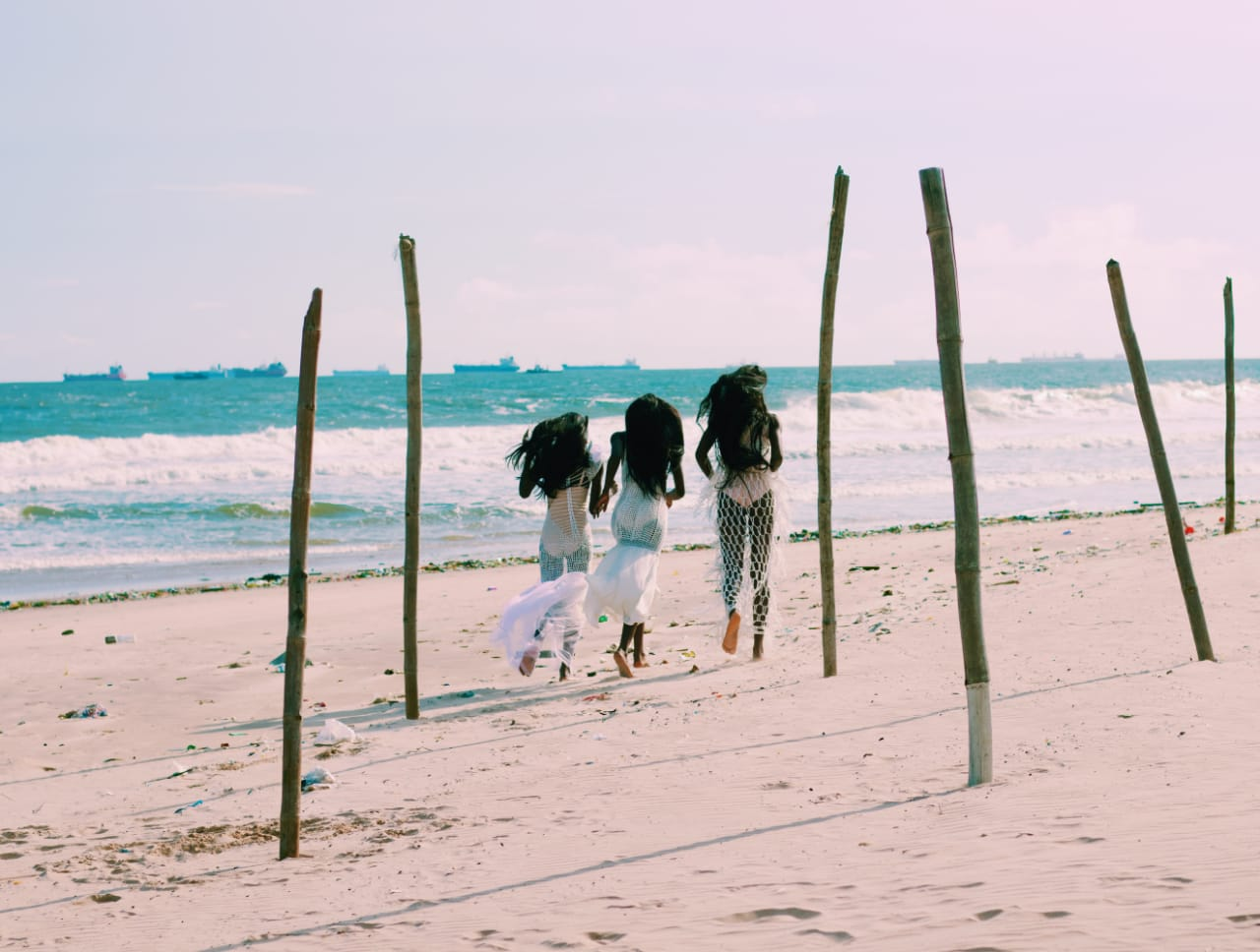 Female models wearing crocheted dresses running by the beach as featured in Pink Noise: a fashion film