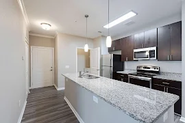 Kitchen with dark brown cabinets, stainless steel appliances, granite countertops, island with sink, grey wood floors