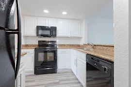 Modern apartment kitchen with white cabinets, granite countertops, and black appliances.