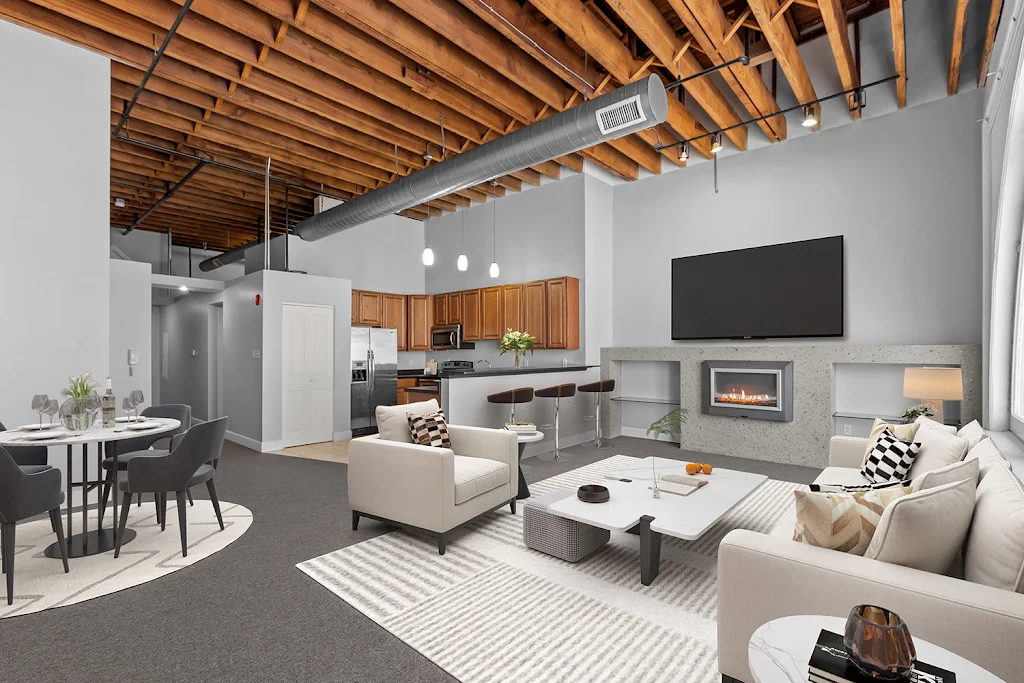 Model apartment living room featuring a sofa, chairs, fireplace, mounted TV and kitchen in the background