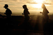 A group of social runners training for a marathon running in Olievenhoutbosch towards Centurion silhouetted by an early morning sunrise. 