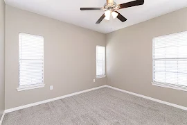 Bedroom with plush carpet, ceiling fan, and three windows