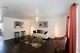 Model unit living area with wood plank flooring, white walls and trim, a couch, a decorative chair and two stools