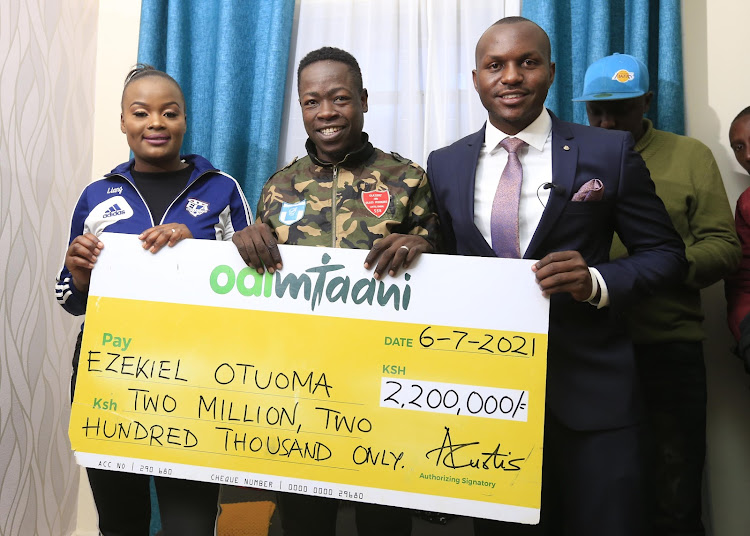 Odibets marketing manager Aggrey Sayi (R) presents a dummy cheque Sh2.2 million to ailing Ezekiel Otuoma and his wife Rachael Otuoma.