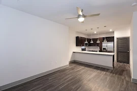 Open concept living room with wood-inspired flooring, neutral colored walls, ceiling fan, and access to the kitchen area