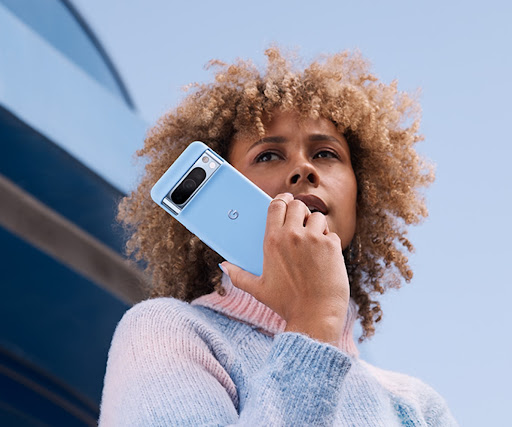 A person gazes around on a hiking trail. In their left hand is a Pixel 8 Pro in a Pixel 8 Pro Case. They also wear a Pixel smartwatch.