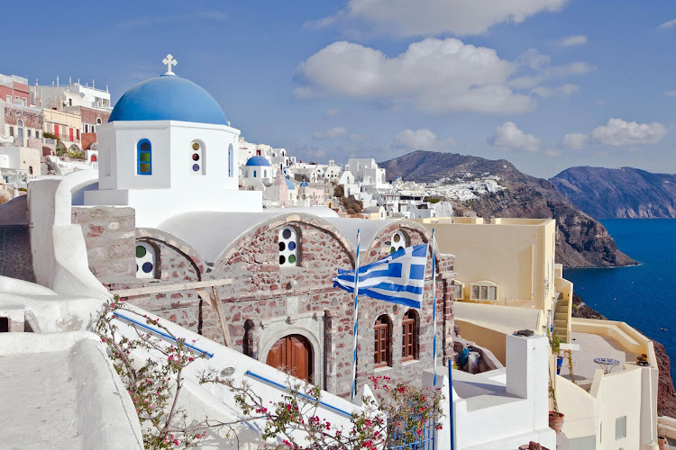 A view of a Greek Orthodox church, with a Greek flag fluttering, in Oia on Santorini, Greece.  