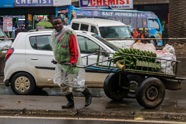 A man pulls a cart covered in polythene paper to shield himself from the rains.